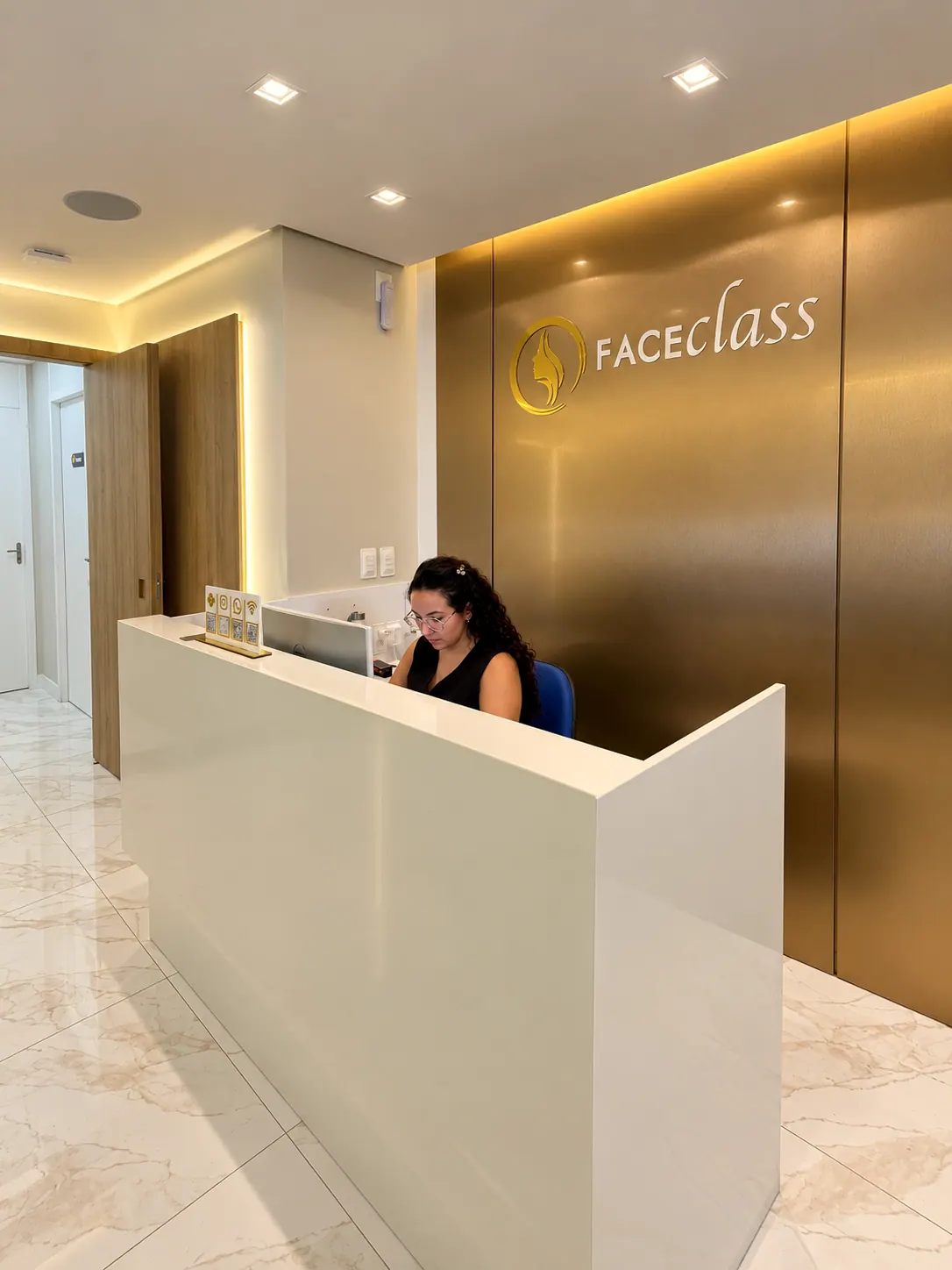 Recepção da Faceclass com balcão branco, piso de mármore e parede dourada