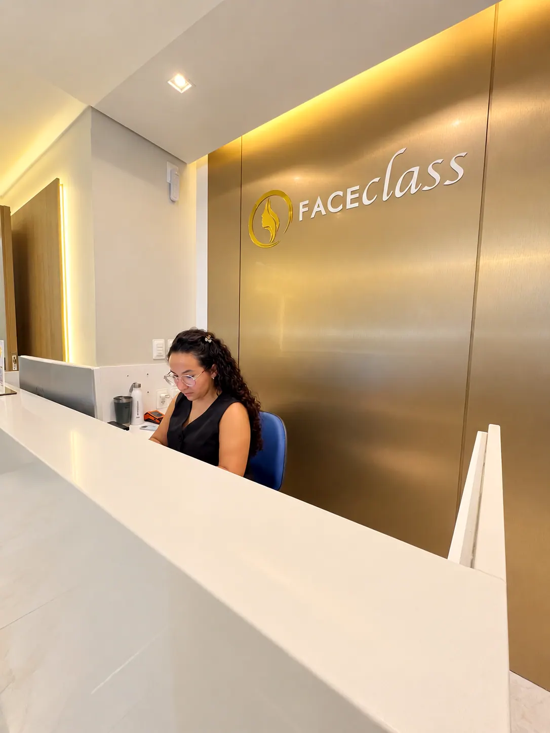 Recepção da Faceclass com parede de metal dourado escovado e o logo da clínica